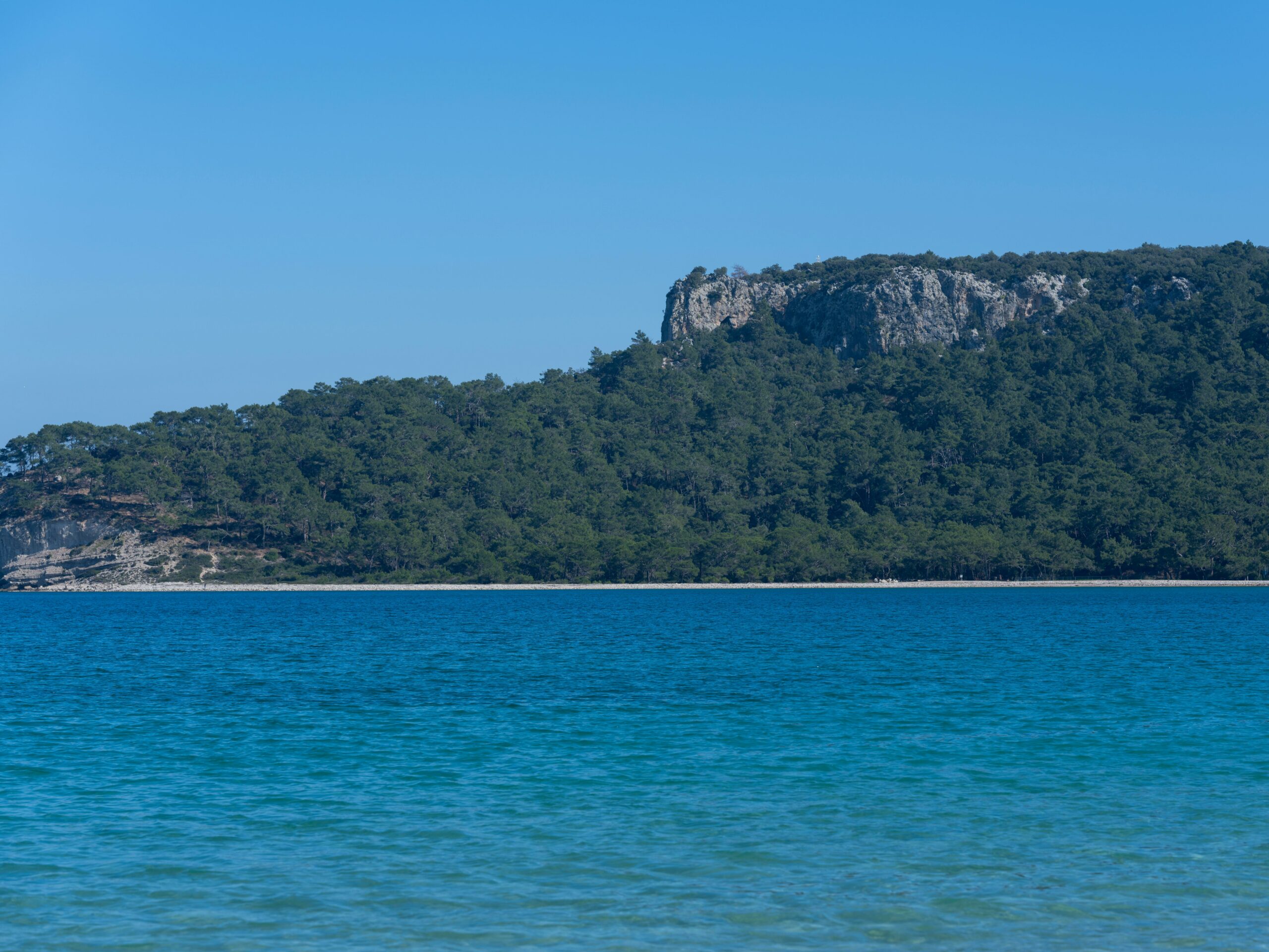 Wunderschöne Küstenlandschaft mit blauem Wasser und üppig bewaldeten Klippen unter klarem Himmel.